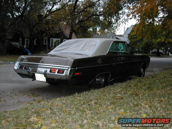 Black 1970 Dodge Dart parked on grassy shoulder, rear view. Covered roof