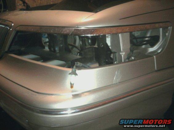 Tan car front end with chrome trim and woodgrain accent above headlight opening
