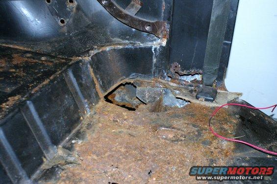 Rusted interior floor pan with seatbelt anchor