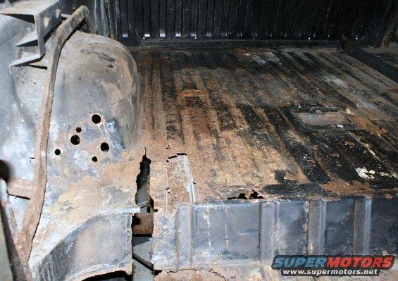 Interior of a rusty vehicle showing floor damage and wheel well