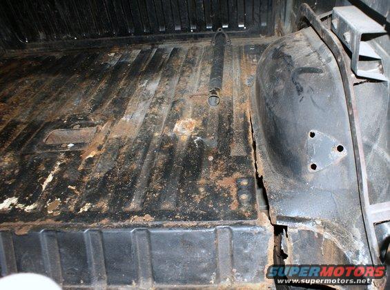 Interior cargo area of a vehicle showing rust and wear on the floor and wheel well