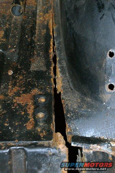 Rusted floor pan seam on a vehicle interior. Visible rust and a large crack