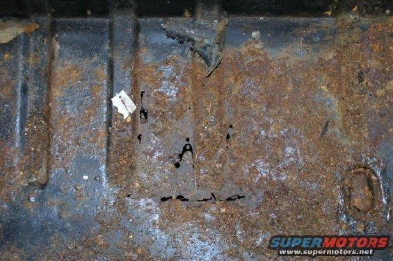 rusted metal floor pan with holes and a small piece of paper stuck to it