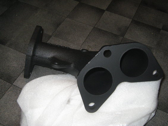 black exhaust manifold with two bolt holes on a flange, sitting on white foam padding