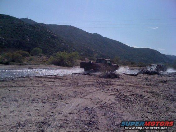 Red pickup truck driving through shallow water, another vehicle in background