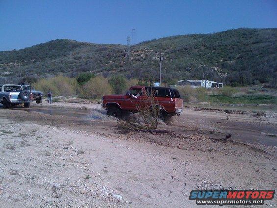 Red 1978 Ford Bronco driving through water, side view