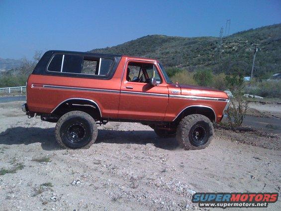 Orange 1978 Ford Bronco side view with black top and off-road tires