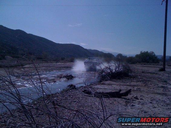 1978 Ford Bronco driving through a shallow stream, kicking up water spray