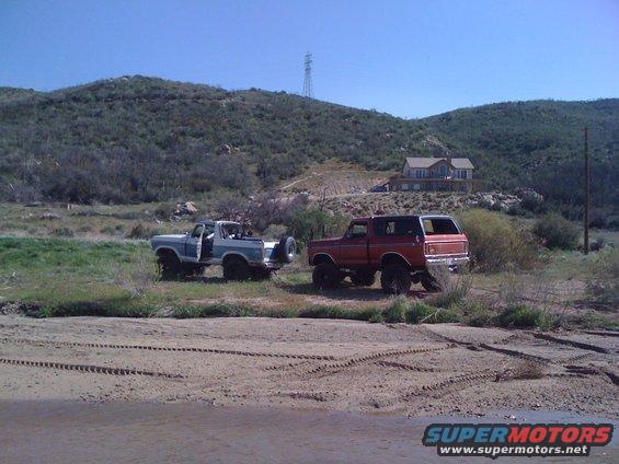 Two 1978 Ford Broncos parked in a dry, grassy area with tire tracks in the foreground