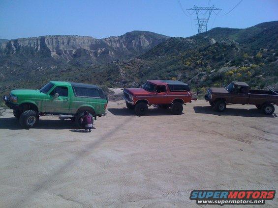 Red 1978 Ford Bronco parked on dirt lot with a green Bronco and brown pickup
