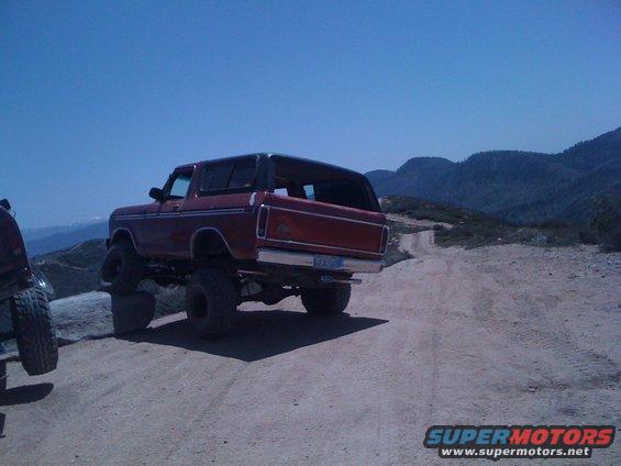 Red 1978 Ford Bronco with black top, lifted suspension, and large tires on a dirt road