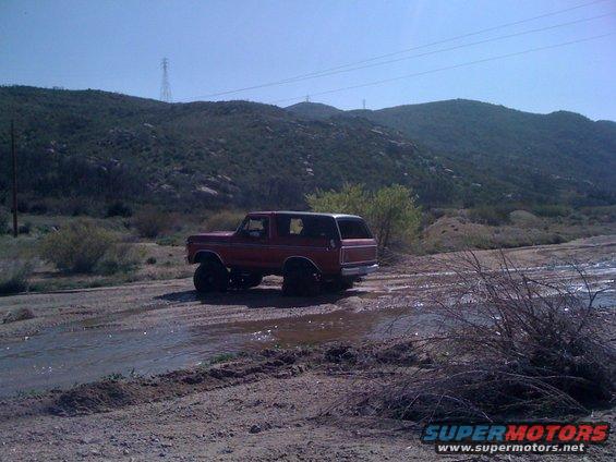 Red 1978 Ford Bronco driving through a stream, 3q-front view