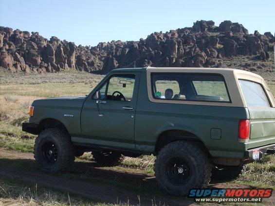 Green Ford Bronco parked on dirt road with rocky hills in background
