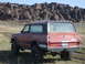 1989 Ford Bronco - A red SUV with a roof rack is parked in a field with a rocky landscape behind it.