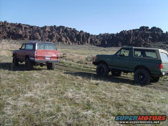 1989 Ford Bronco and a red SUV parked on a grassy hill