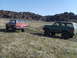 1989 Ford Bronco - Two SUVs, one green and one red, are parked on a grassy hill with rocky formations behind them.