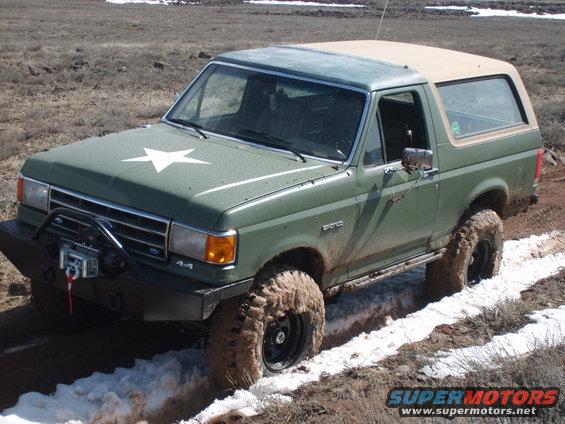 Green Ford Bronco with a white star on the hood driving through mud and snow