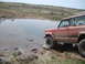1989 Ford Bronco - Jeep Cherokee XJ navigates off-road terrain near a water obstacle.