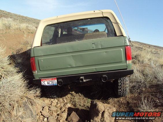 Green Ford Bronco with tan top on rocky terrain, rear view