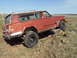 1989 Ford Bronco - A red Jeep Cherokee Chief navigates rocky terrain on a sunny day.