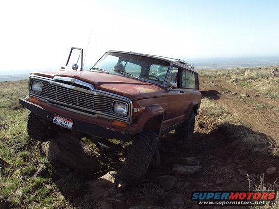 Red Jeep Wagoneer with door open, navigating rocky terrain