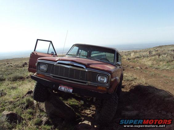 1984 Jeep Wagoneer with driver's door open, climbing over rocks on a dirt trail