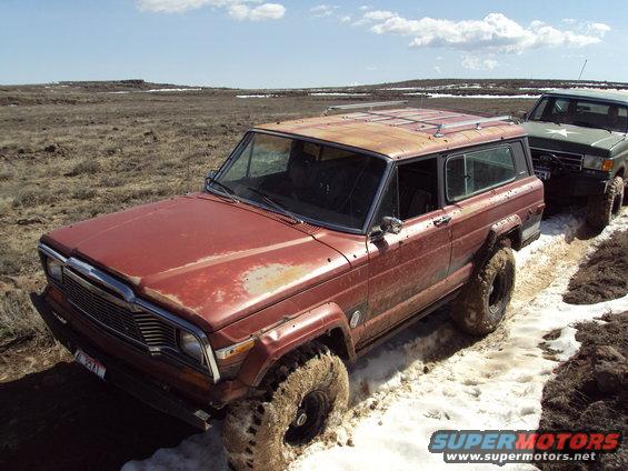 Red Jeep Grand Wagoneer stuck in mud and snow, another vehicle behind it