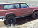 1989 Ford Bronco - This red SUV, identified by its "Cherokee" badging, is equipped with off-road tires and navigates a muddy trail.