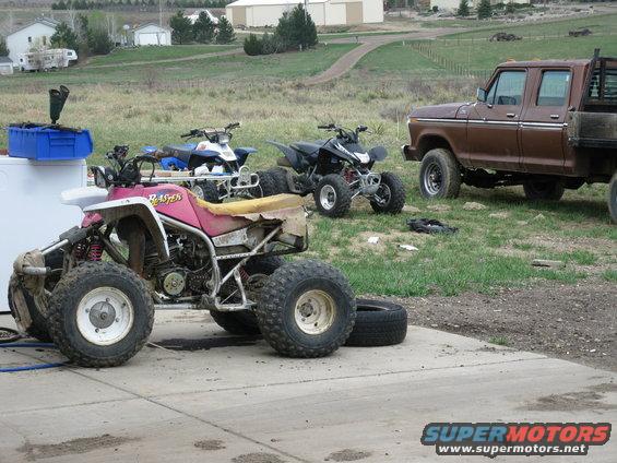 Three ATVs and a brown pickup truck parked in a yard