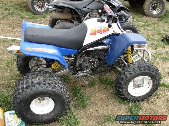 Blue and white Yamaha Blaster ATV parked on dirt and grass. Another ATV is visible behind it