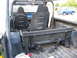 1973 Ford Bronco - Modified interior of an off-road vehicle, racing seats and a roll cage, with a blue pickup truck visible in the background.