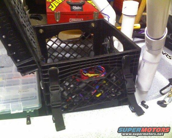 Black milk crate with fishing tackle and PVC pipes attached, red toolbox in background