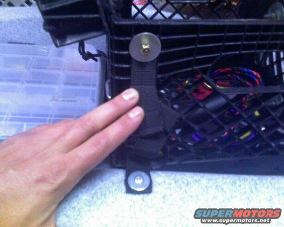 Hand holding a strap attached to a black basket with wires inside. Storage containers are to the left