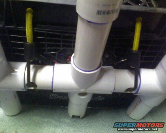 PVC pipe structure with yellow cords attached to black clips, resting on a black grate