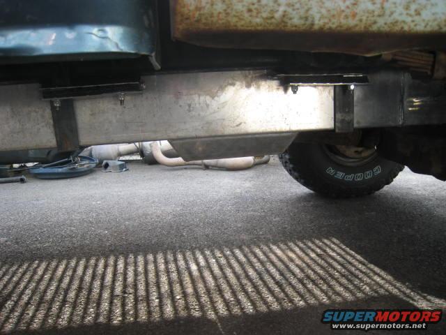 Side view of a truck's undercarriage, showing a metal fuel tank and exhaust pipes
