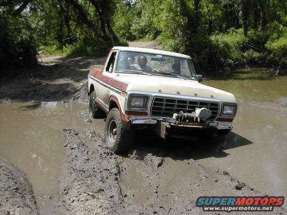 Ford F-Series truck driving through mud and water, with people inside