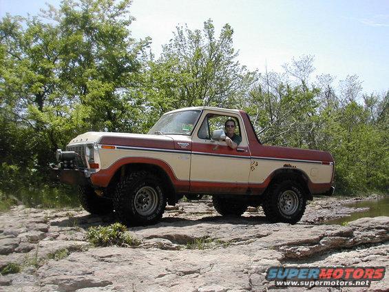 Ford Bronco with two-tone paint parked on rocks near water, driver visible