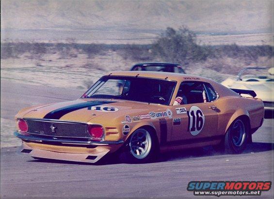 Orange race car with black stripe and number 16, low front splitter, racing on a track