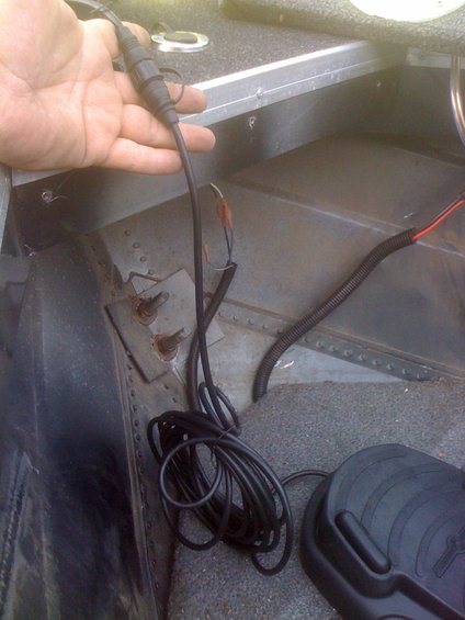 Hand holding a black electrical connector with coiled black wire and red/black wires connected to terminals inside a boat