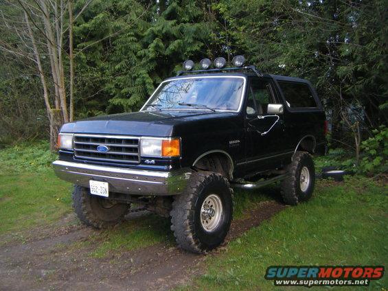 Black lifted 1990 Ford Bronco with roof lights and off-road tires parked on grass