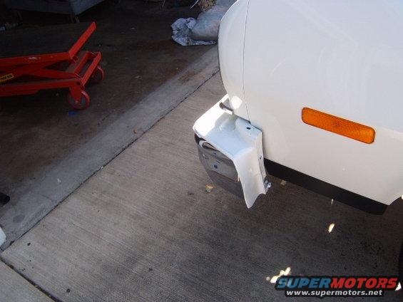 White vehicle's damaged front bumper corner, showing exposed metal and white plastic trim