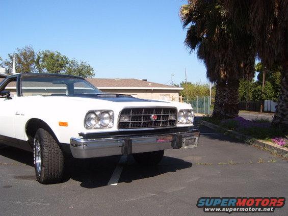 White coupe utility with a black hood scoop parked outside with palm trees and a building in the background