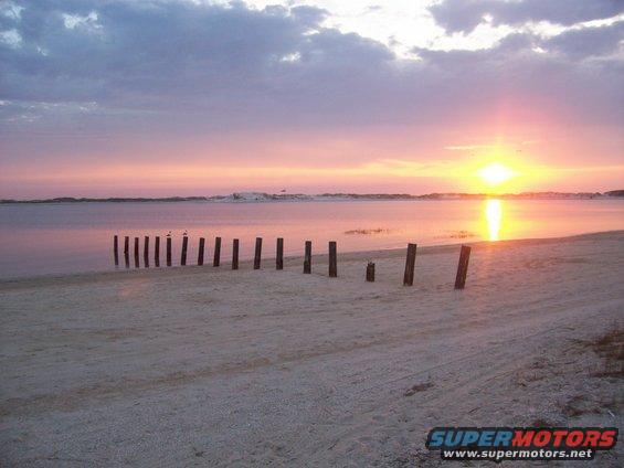 Beach scene with wooden posts and sunset over water