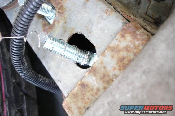 Close-up of a bolt going through a rusty metal frame with black corrugated tubing nearby. Supermotors.net logo visible