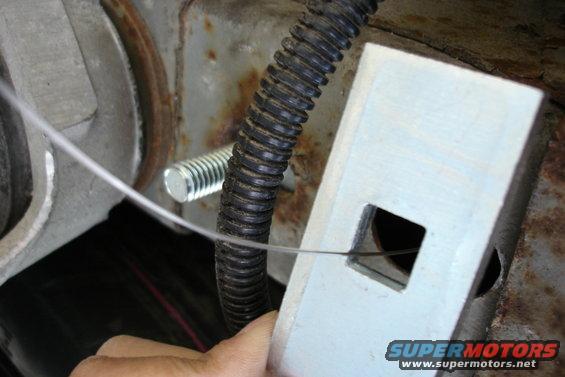 Trailer hitch mounting bracket with a wire and a bolt. A hand is visible