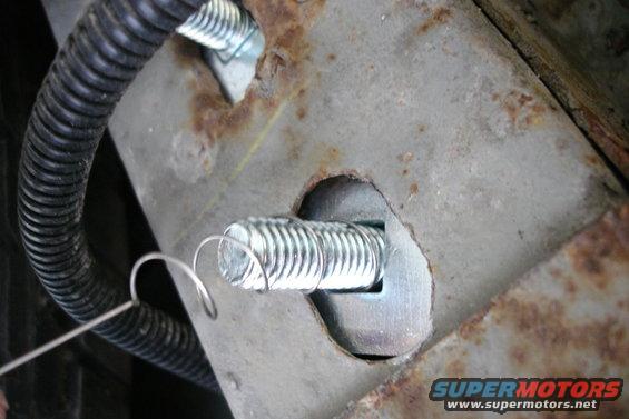 Close-up of rusted metal with two bolts and a black corrugated wire loom. Supermotors.net logo visible