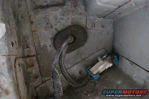 Close-up of a vehicle's wiring harness and electrical connector, showing some rust on the surrounding metal