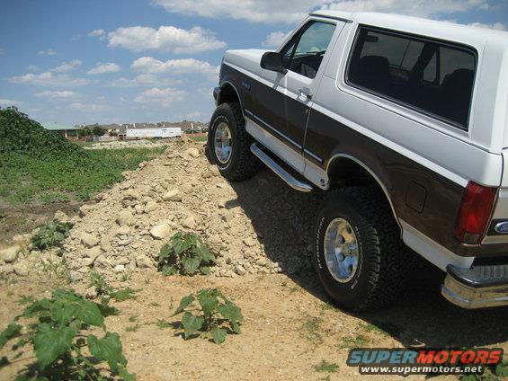 White and brown 1993 Ford Bronco with lift and tires on dirt mound