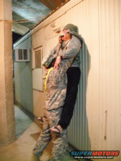 Two individuals in camouflage uniforms embracing near a corrugated wall