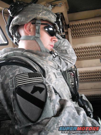 Soldier in camouflage uniform and helmet, wearing sunglasses, inside a vehicle